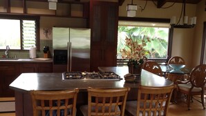 A kitchen with a central island, wooden chairs, a refrigerator, and a window with a view of greenery. - Magical 4 Bedroom 3 Bath Home with Awesome Mountain View's. New Full house AC (Princeville)