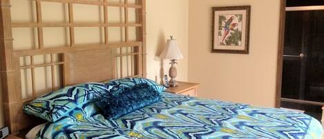 A bedroom with a bed, a nightstand, a lamp, a framed picture, and a window.