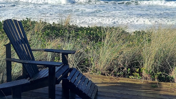 Una terraza de madera con dos sillas Adirondack orientadas al océano.