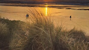 Escena de playa con atardecer, olas y gente caminando.