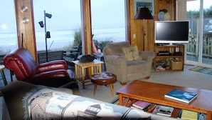 Una sala de estar con un sillón de cuero, un sillón beige, una mesa de centro de madera y un televisor sobre un mueble.