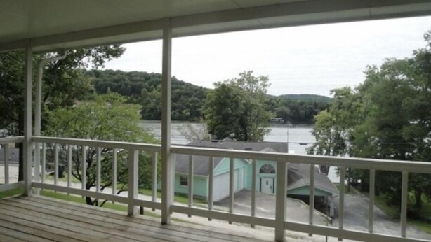 A covered porch with a view of a lake and a building with a green roof. - Cute and cozy. Located in a very quiet street.   (Camdenton)