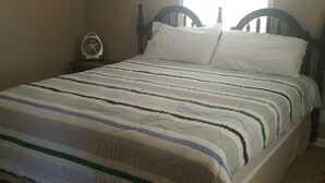 A bed with a striped bedspread, a bedside table with a fan, and a wooden headboard. - Cute and cozy. Located in a very quiet street.   (Camdenton)