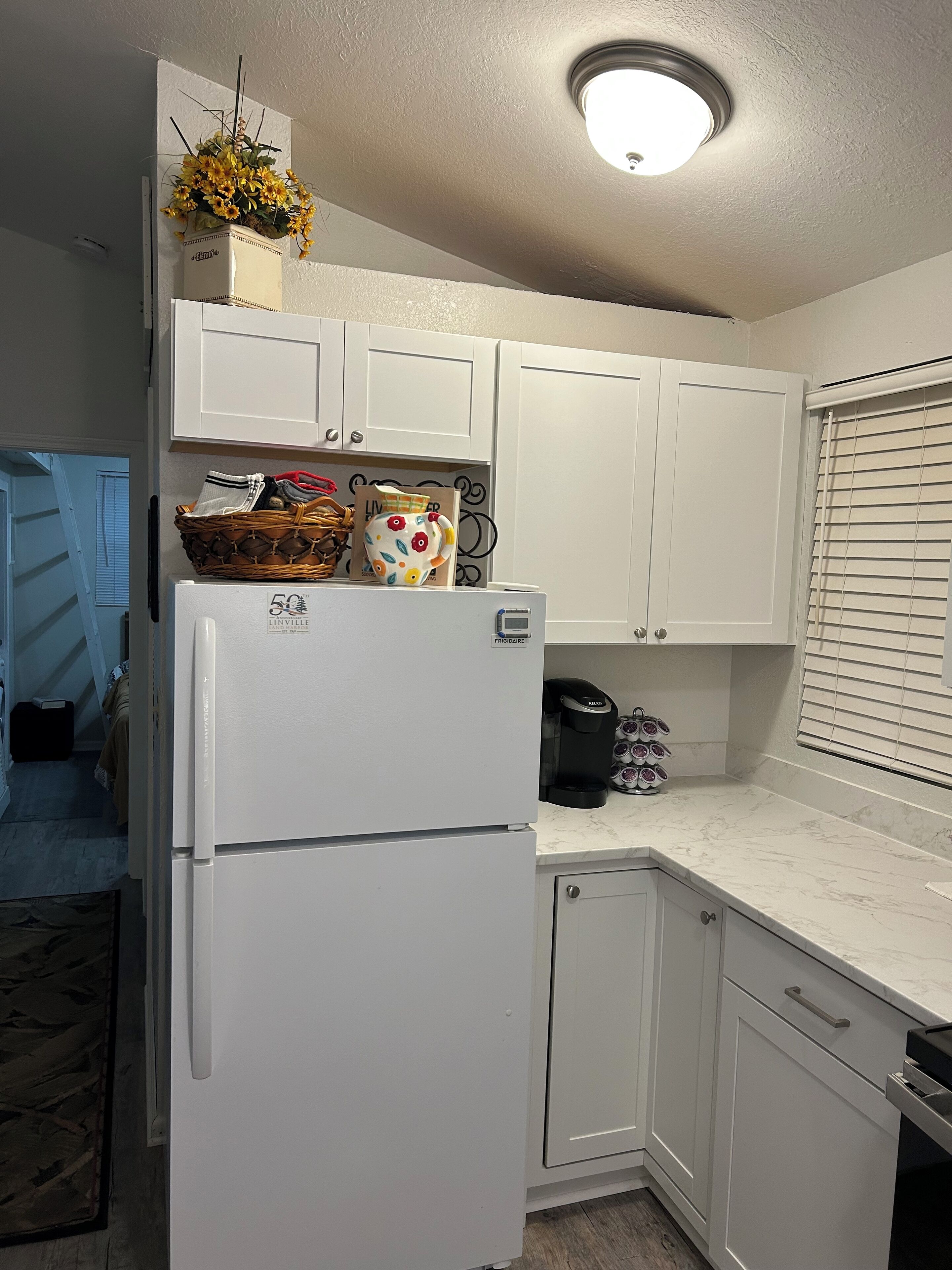 A kitchen with white cabinets, a refrigerator, a coffee maker, and a basket with flowers on top.