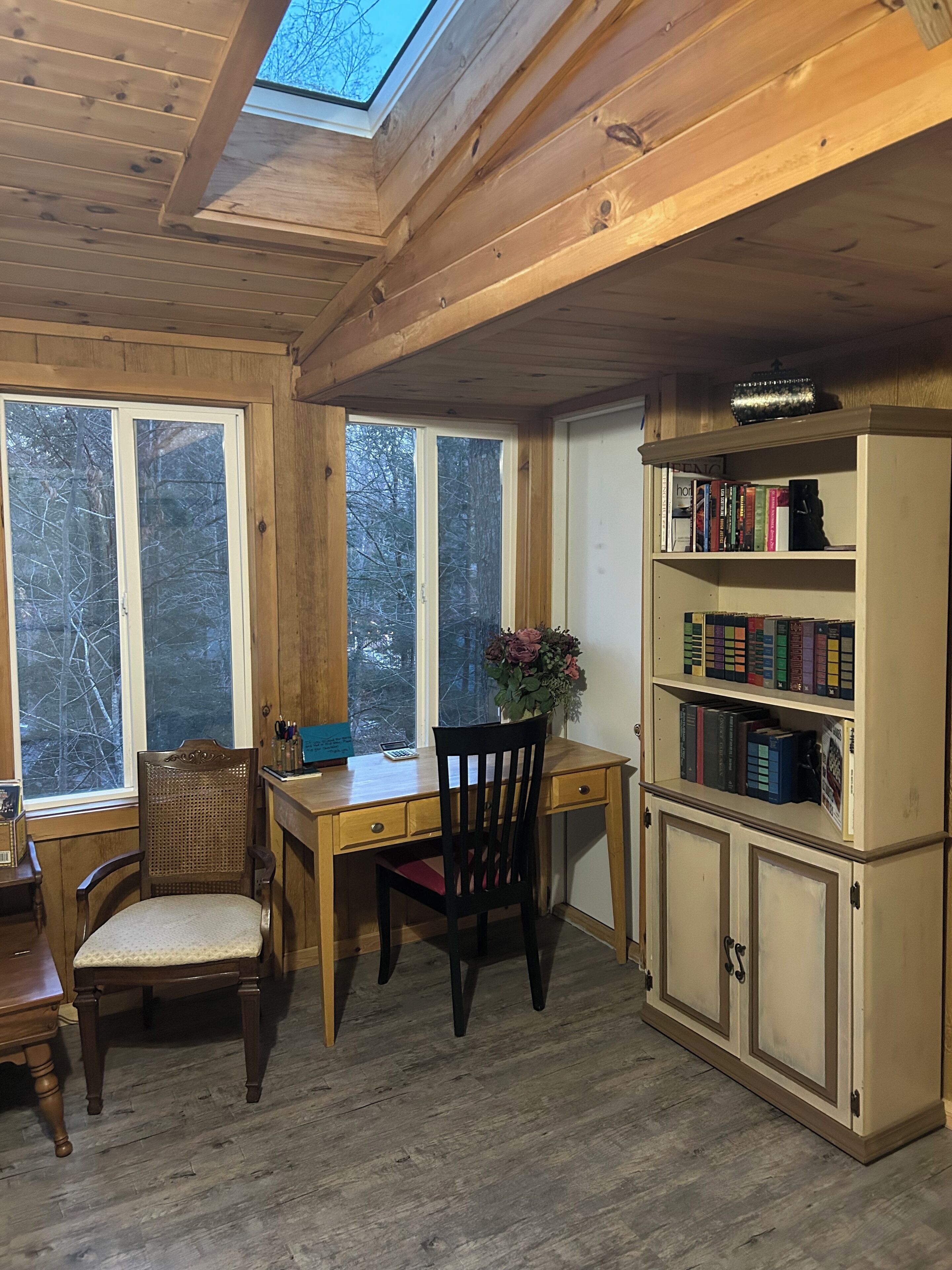 Un interno in legno con una scrivania, una sedia, una libreria e un lucernario.