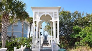 A white gazebo with a staircase leading up to it, surrounded by palm trees and a white picket fence.