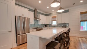 A modern kitchen with white cabinetry, stainless steel appliances, a central island with bar stools, and pendant lighting.