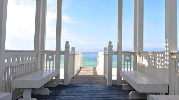 A wooden pier with white railings leading to a beach.