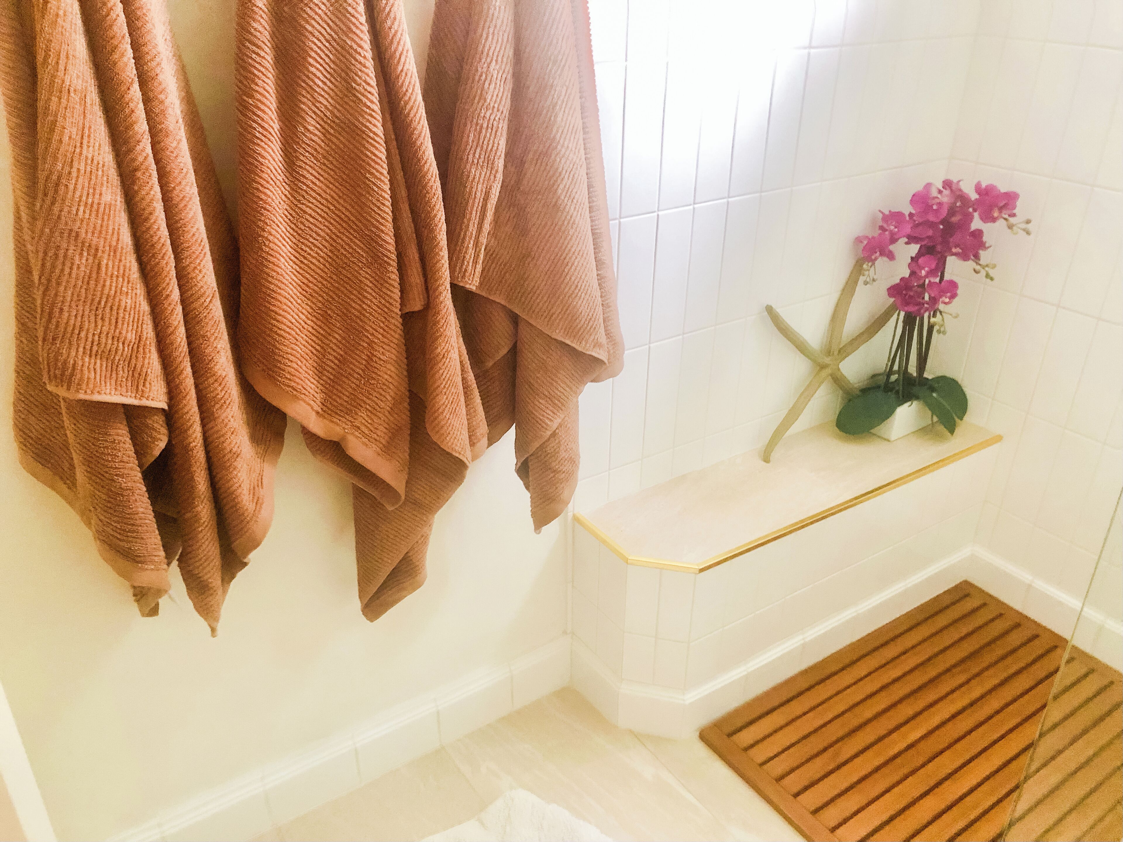 Ein Badezimmer mit Handtüchern an einem Halter, einer kleinen Ablage mit einer Meerstern-Dekoration und einer Holzmatte auf dem Boden.