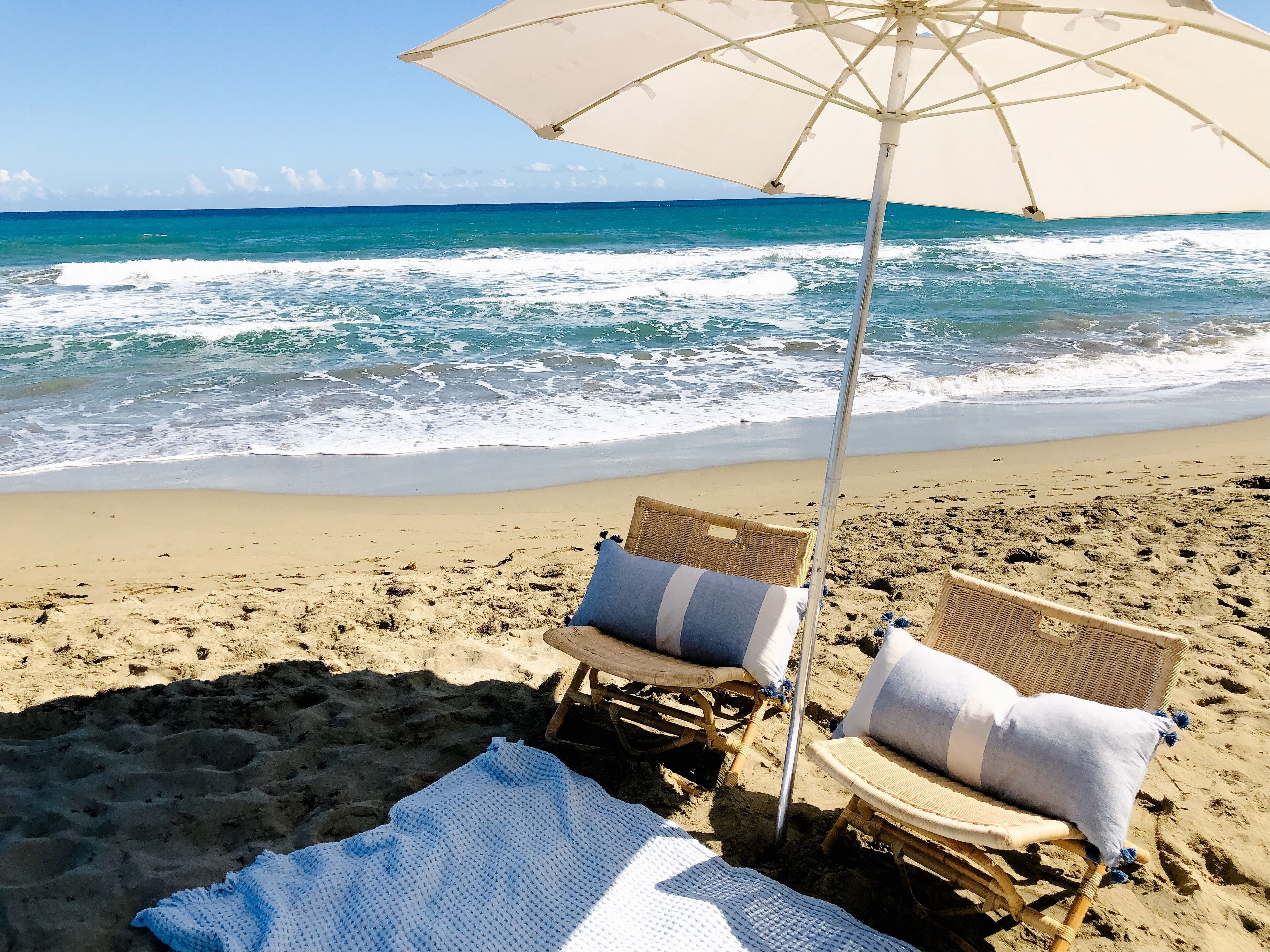 A beach scene with two wicker chairs and a large umbrella, positioned on a sandy beach with the ocean in the background.