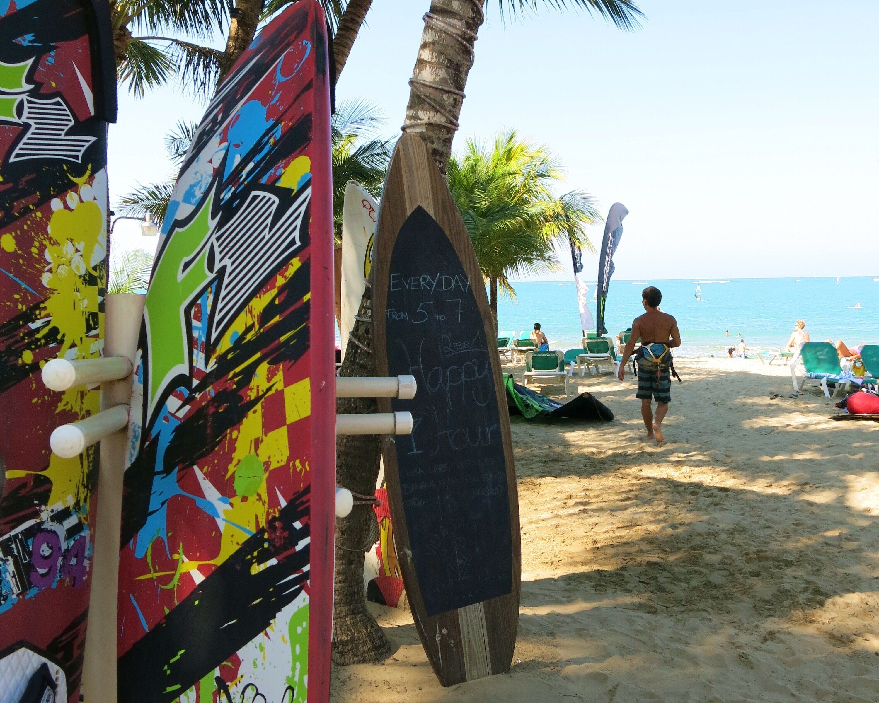 Ein Strand mit Surfbrettern, die an einem Pfahl lehnen, einer Tafel mit Schrift und Liegestühlen.