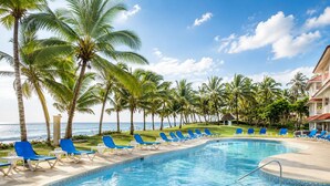 Une piscine bordée de chaises bleues, de palmiers et offrant une vue sur l’océan.