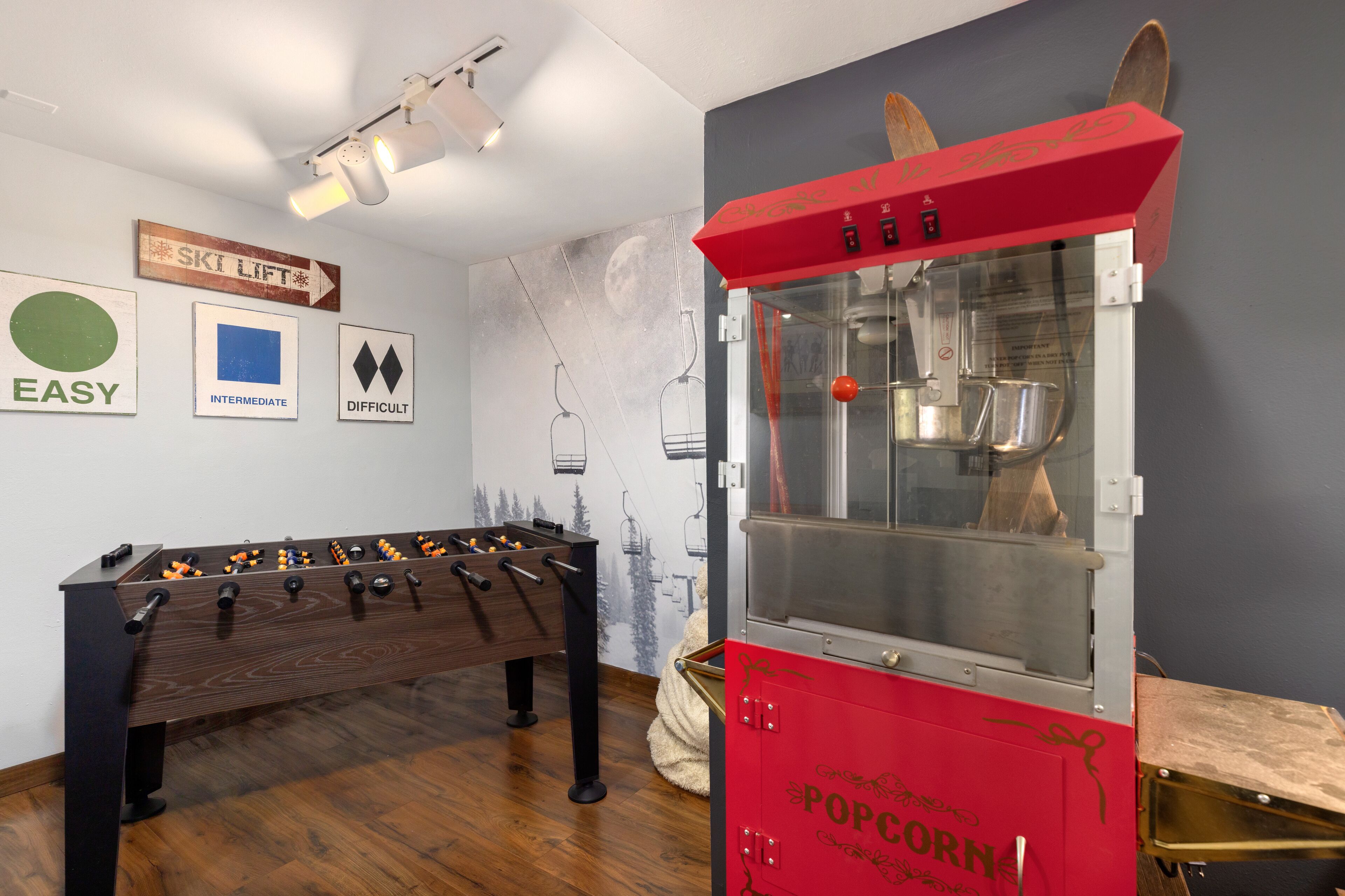A room with a foosball table, a popcorn machine, and wall decorations including a 'SKILIFT' sign and difficulty level signs.