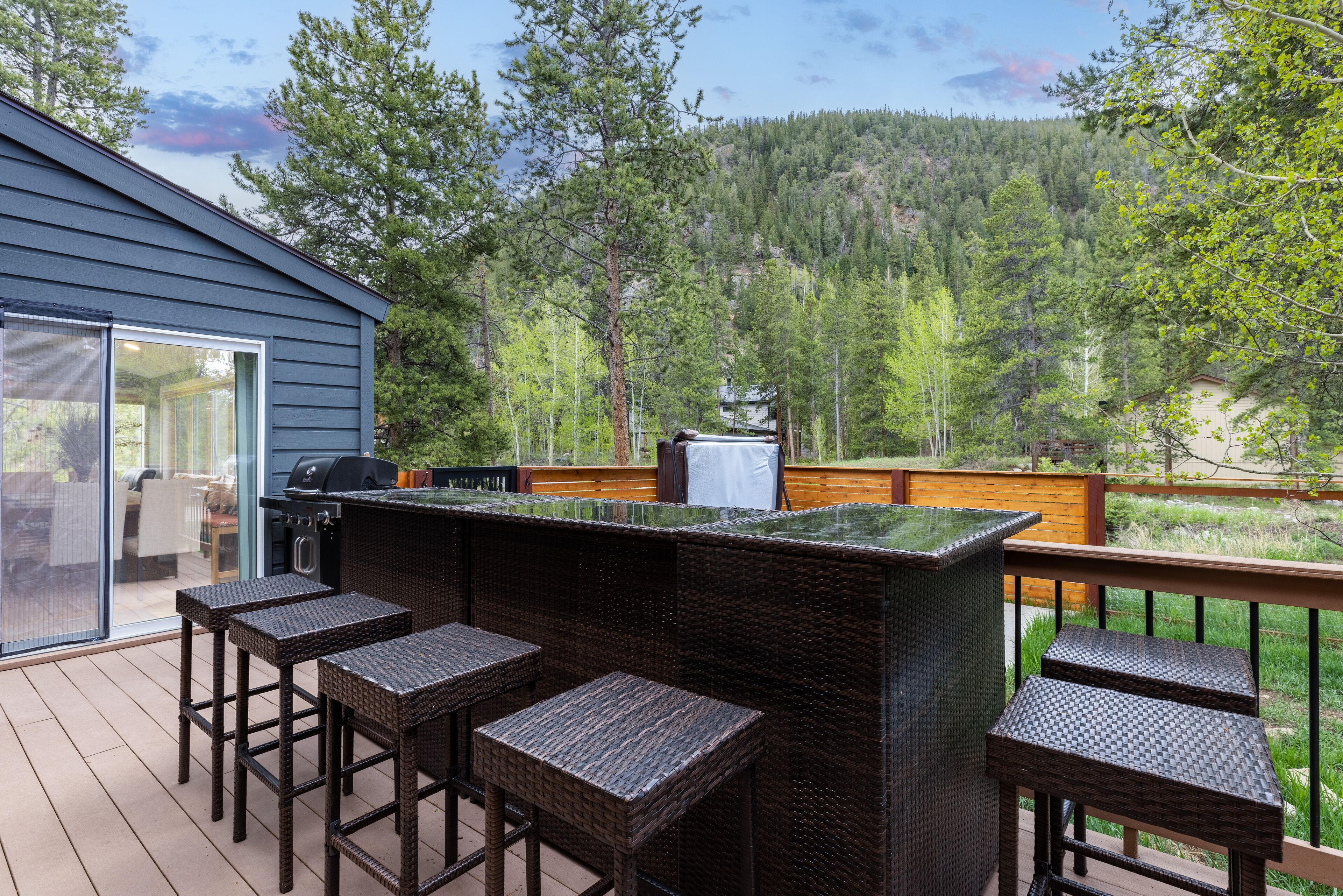 An outdoor deck with wicker furniture, a grill, and a view of a forested hillside.