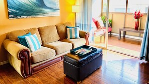 Un salón con sofá, reposapiés y un cuadro de una ola.