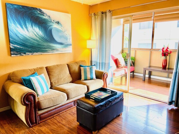 A living room with a sofa, ottoman, and a painting of a wave.