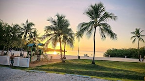 Eine Strandlandschaft mit Palmen, einem Spielplatz und einem Sonnenuntergang.