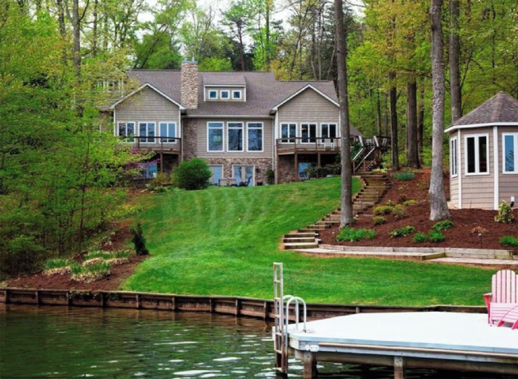 A large house with a dock and red chairs by the water.