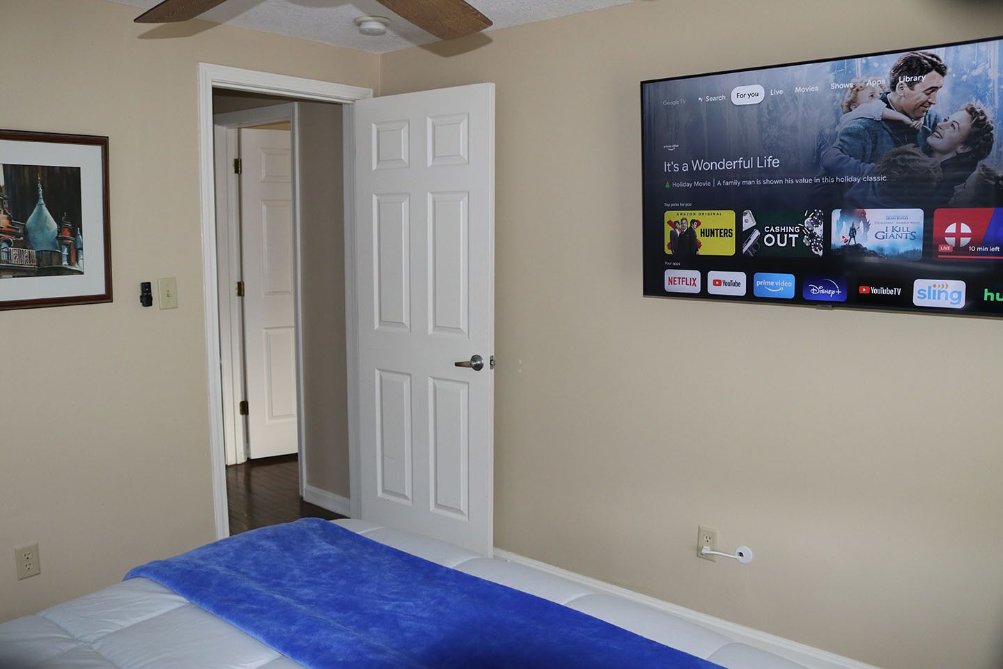 Ein Hotelzimmer mit einem Bett, einer Tür und einem an der Wand befestigten Fernseher, der verschiedene Streaming-Dienste anzeigt.