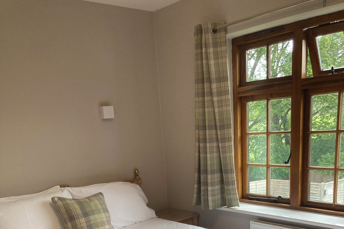 A neatly made bed in a room with a large window, a radiator, and a small bedside table.