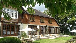 A traditional wooden building with a well-maintained lawn and outdoor seating area. - Tottington Manor (Henfield)