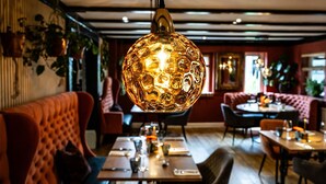 A restaurant interior with a round, textured hanging light fixture, wooden tables, and cushioned seating. - Tottington Manor (Henfield)