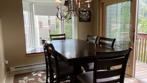 A dining area with a large table and chairs, a chandelier, and a view through a sliding glass door. - Snowcreek Condo at Sugarbush Resort-2 beds/2 baths, slopeside (Warren)