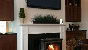 A living room with a fireplace, a television mounted above it, wooden cabinets, and a red carpet. - Snowcreek Condo at Sugarbush Resort-2 beds/2 baths, slopeside (Warren)