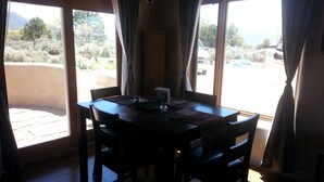 A dining area with a table and chairs, large windows with curtains, and a view of the outdoors. - New adobe guest house - mountain views - great location - hot tub (El Prado)