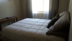 A bed with a white duvet and two pillows, a wooden nightstand, and a window with curtains. - New adobe guest house - mountain views - great location - hot tub (El Prado)