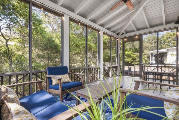 A covered outdoor seating area with a view of trees, a ceiling fan, and a table with chairs.
