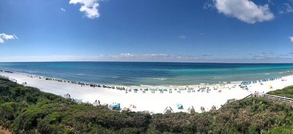 A beach with white sand, clear blue water, and a few umbrellas.