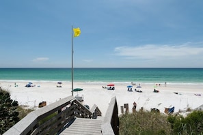 A wooden boardwalk leading to a beach with umbrellas and beach chairs.