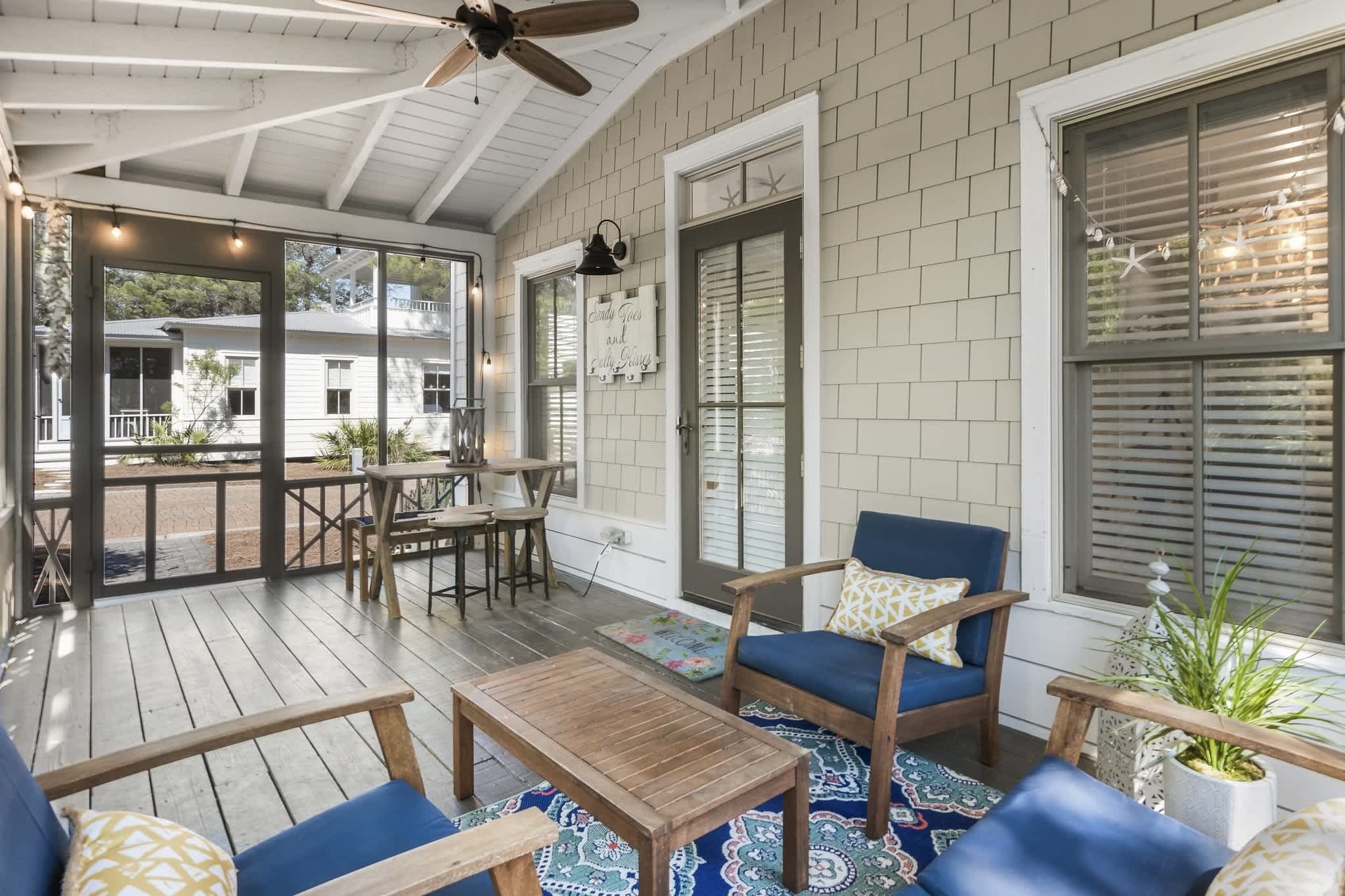 A covered outdoor patio with wooden furniture, a ceiling fan, and a view of a white building in the background.