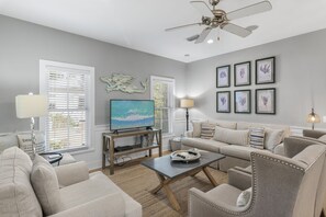 A living room with a sofa, armchairs, a coffee table, a TV, and a ceiling fan. - Beach Chairs, Bikes & Across From Beach! ~ Seas The Day in Magnolia Cottages on 30A (Seacrest Beach)