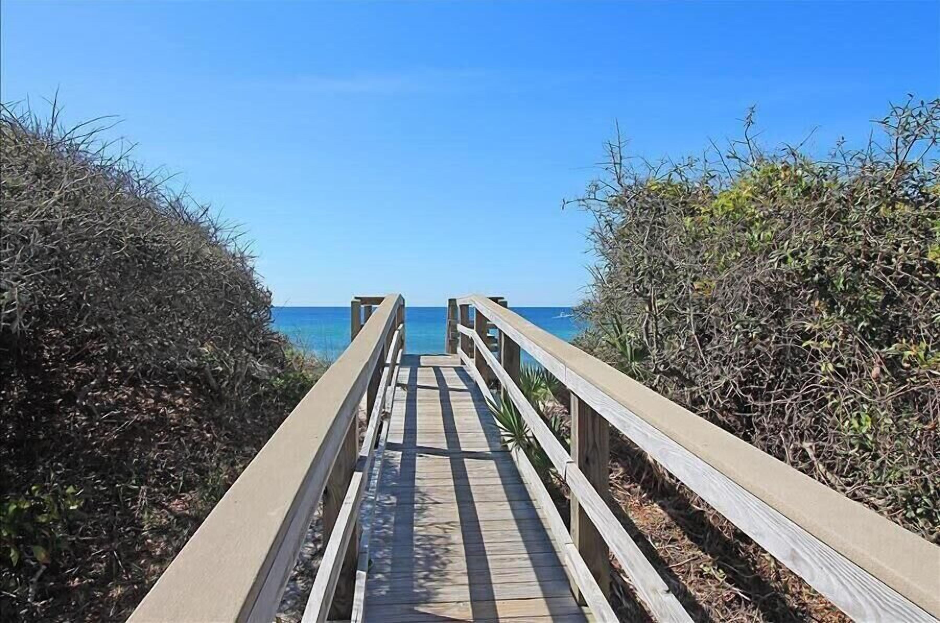 A wooden boardwalk leading to the beach, surrounded by dense shrubbery.