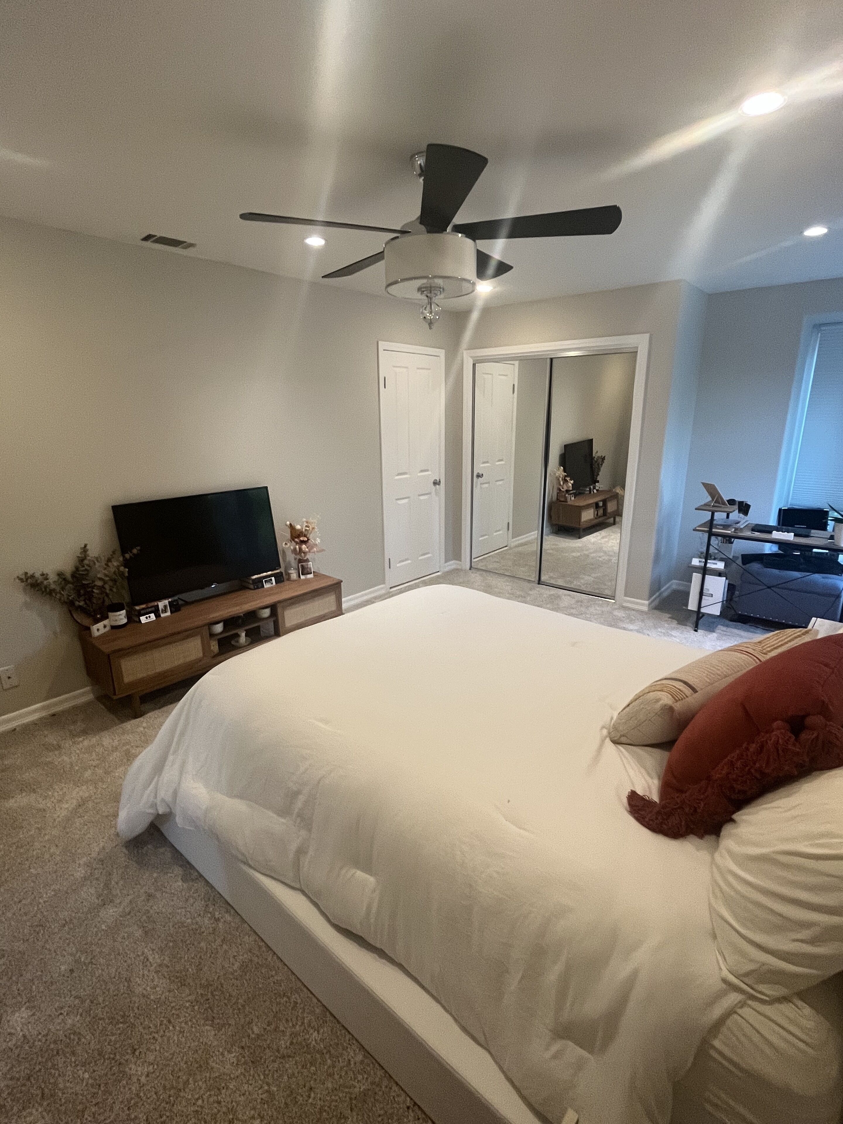 A bedroom with a large bed, a ceiling fan, a TV on a wooden stand, and a closet with a mirror.