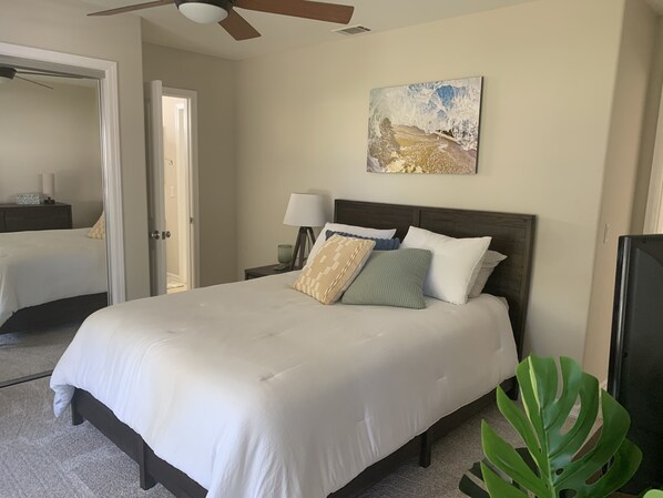 Una habitación de hotel con una cama grande, un ventilador de techo, un cuadro en la pared y una planta.