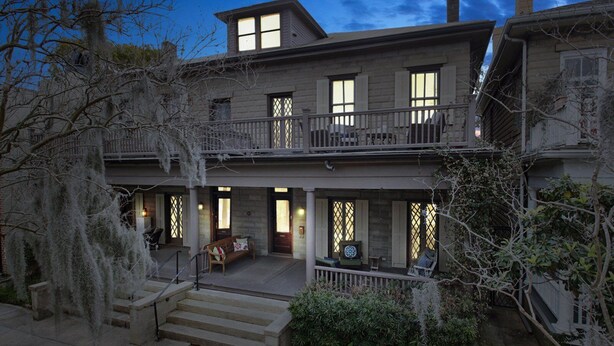 A two-story house with a balcony, a porch with seating, and a staircase leading to the entrance.