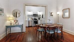 A dining area with a wooden table and chairs, a blue console table with a lamp, and a kitchen in the background.