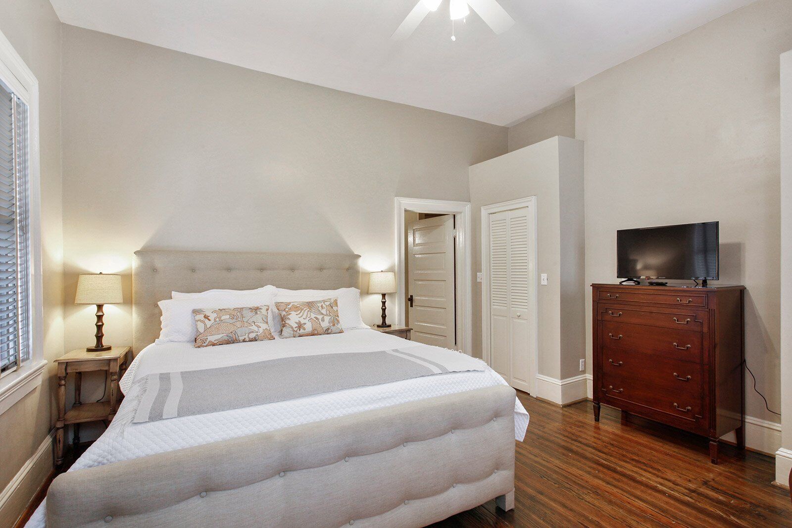 A bedroom with a large bed, two bedside tables with lamps, a dresser, and a television on top.