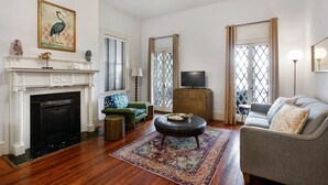 A living room with a fireplace, a television on a wooden cabinet, a green armchair, a grey sofa, and a patterned rug.