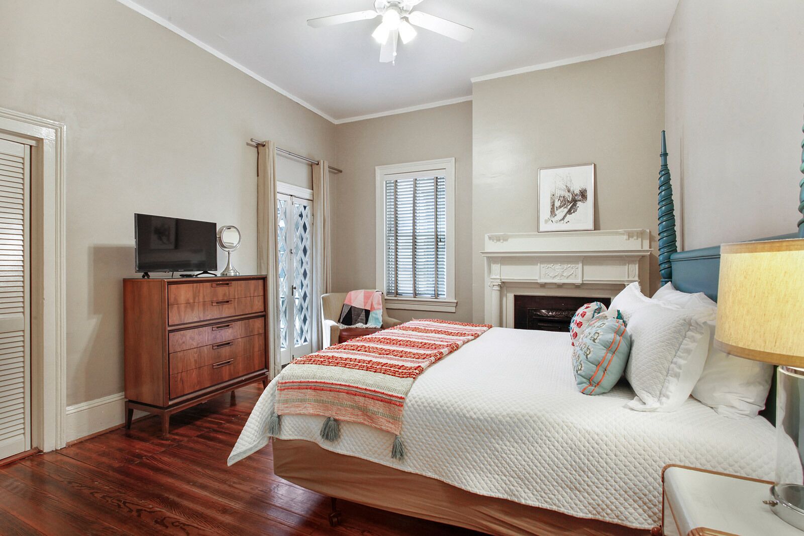 A bedroom with a bed, a dresser, a television, a fireplace, and a window with blinds.