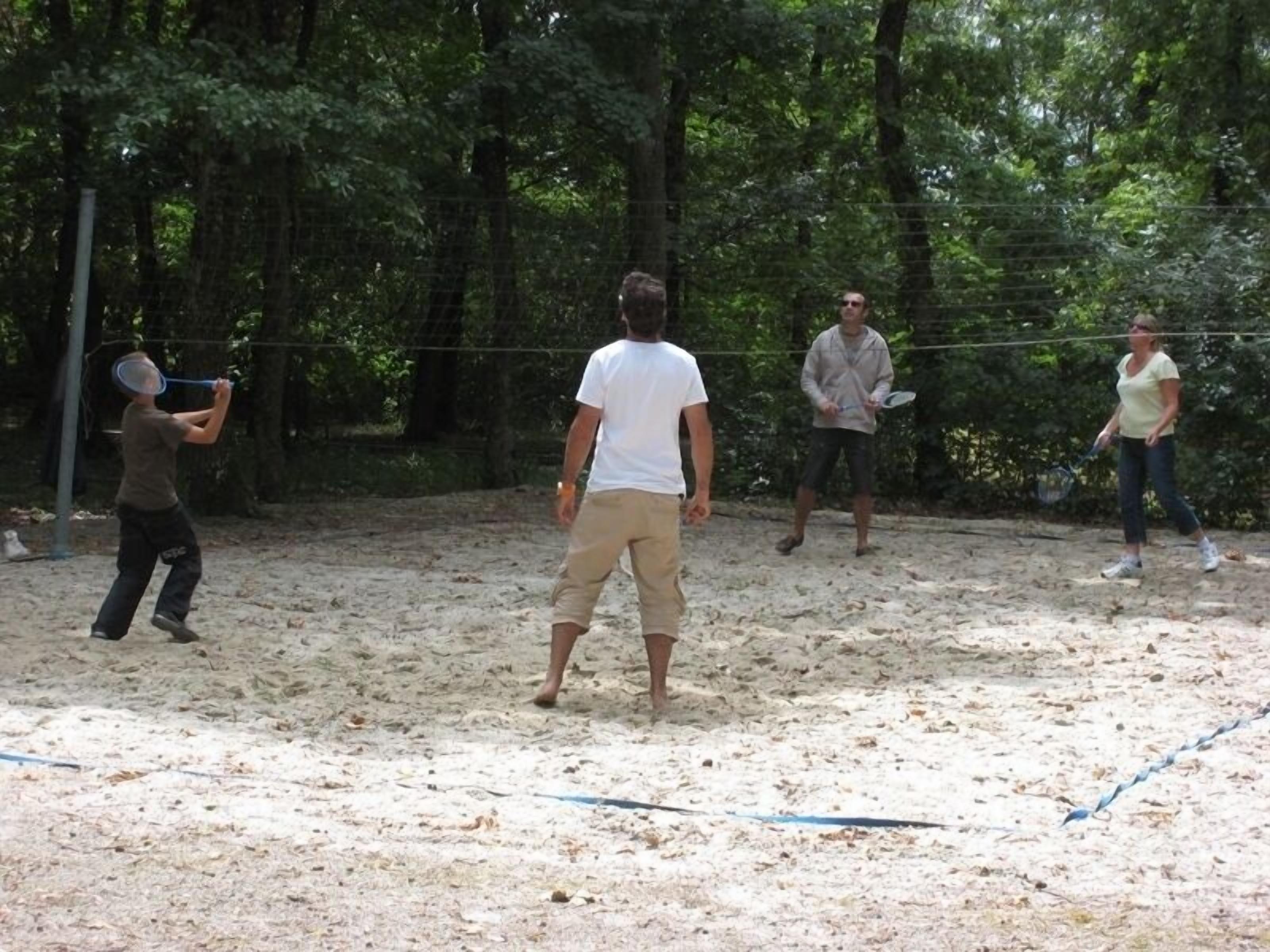 Un espace extérieur sablonneux avec un filet de volley-ball, entouré d’arbres.