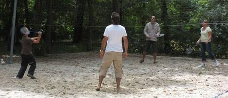Un espace extérieur sablonneux avec un filet de volley-ball, entouré d’arbres.