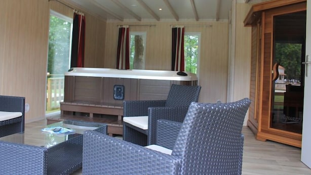 A cozy indoor seating area with wicker furniture, a hot tub, and large windows with curtains. - Les chalets de la héronnière (Chef-Boutonne)