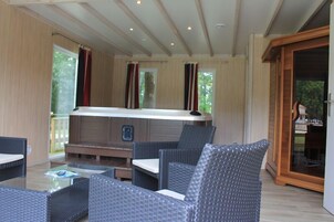 Un espace de détente intérieur, chaleureux, avec des meubles en osier, un jacuzzi et de grandes fenêtres dotées de rideaux.