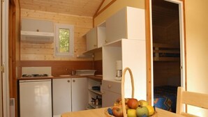 A compact kitchen with a refrigerator, a sink, and a window. A basket of fruit is on the table. - Les chalets de la héronnière (Chef-Boutonne)