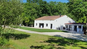 A white building with a red roof, a covered patio with outdoor seating, and a grassy area in front. - Les chalets de la héronnière (Chef-Boutonne)