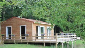 A wooden cabin with two open doors, a covered deck, and potted plants. - Les chalets de la héronnière (Chef-Boutonne)